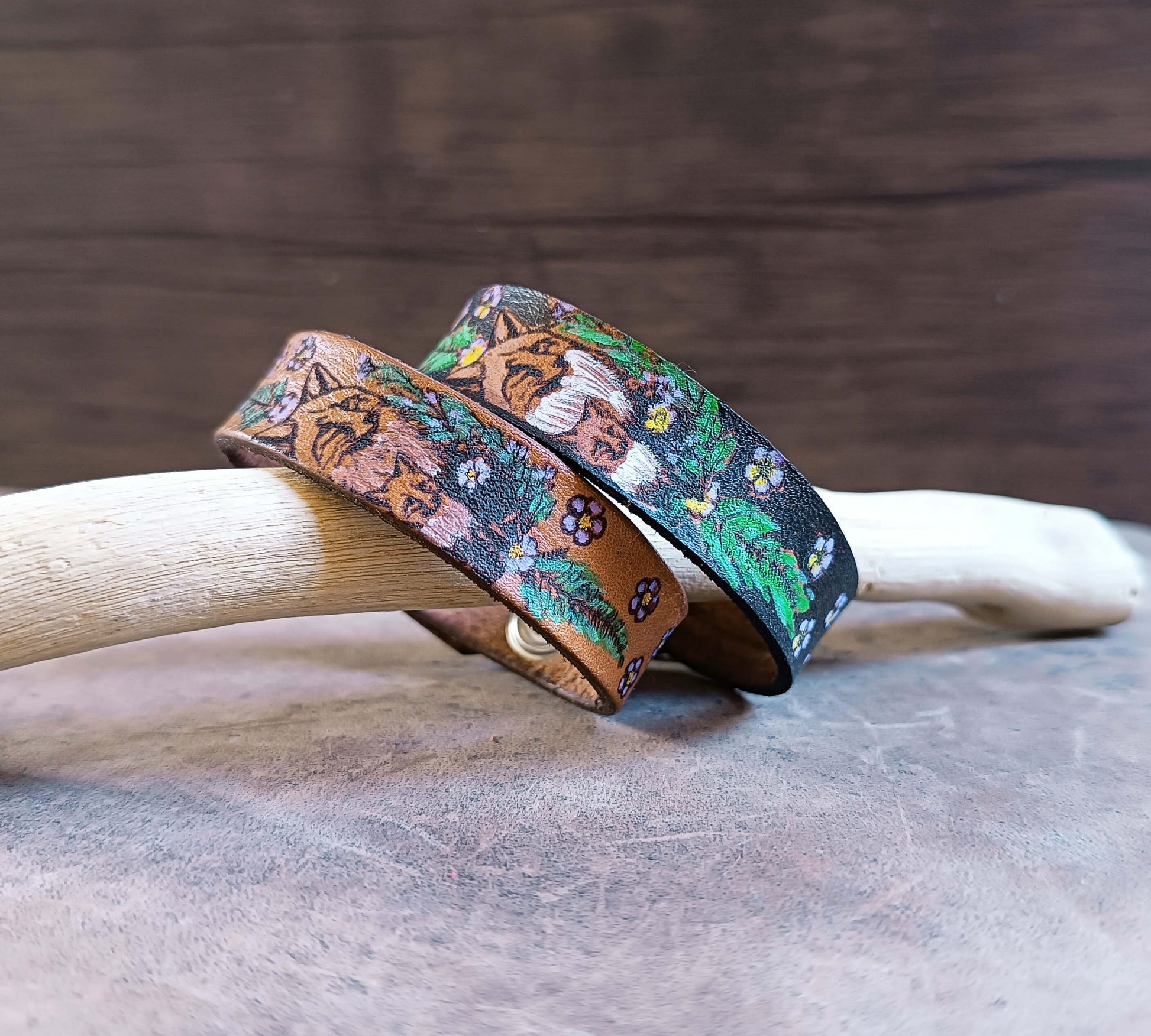 Two leather bracelets with hand painted floral fox designs on a wooden surface