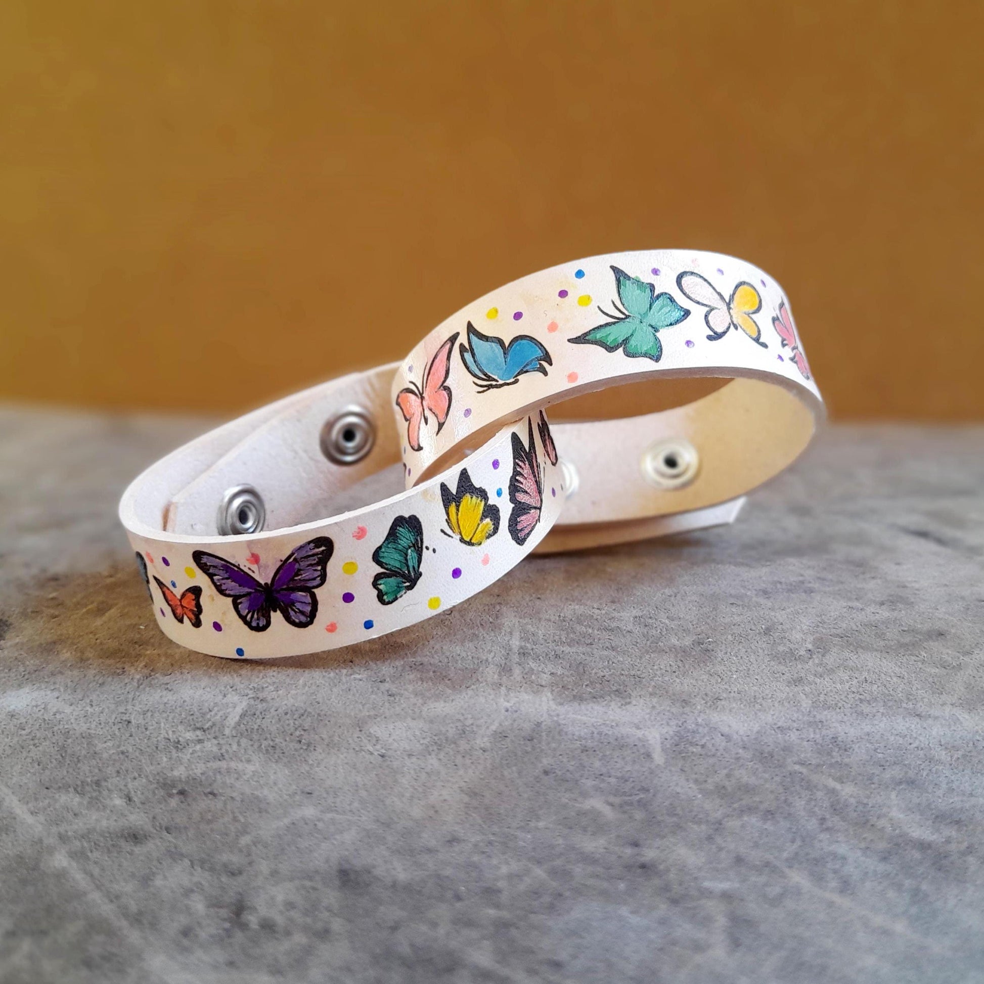 close up of both hand painted leather bracelets with colorful butterflies