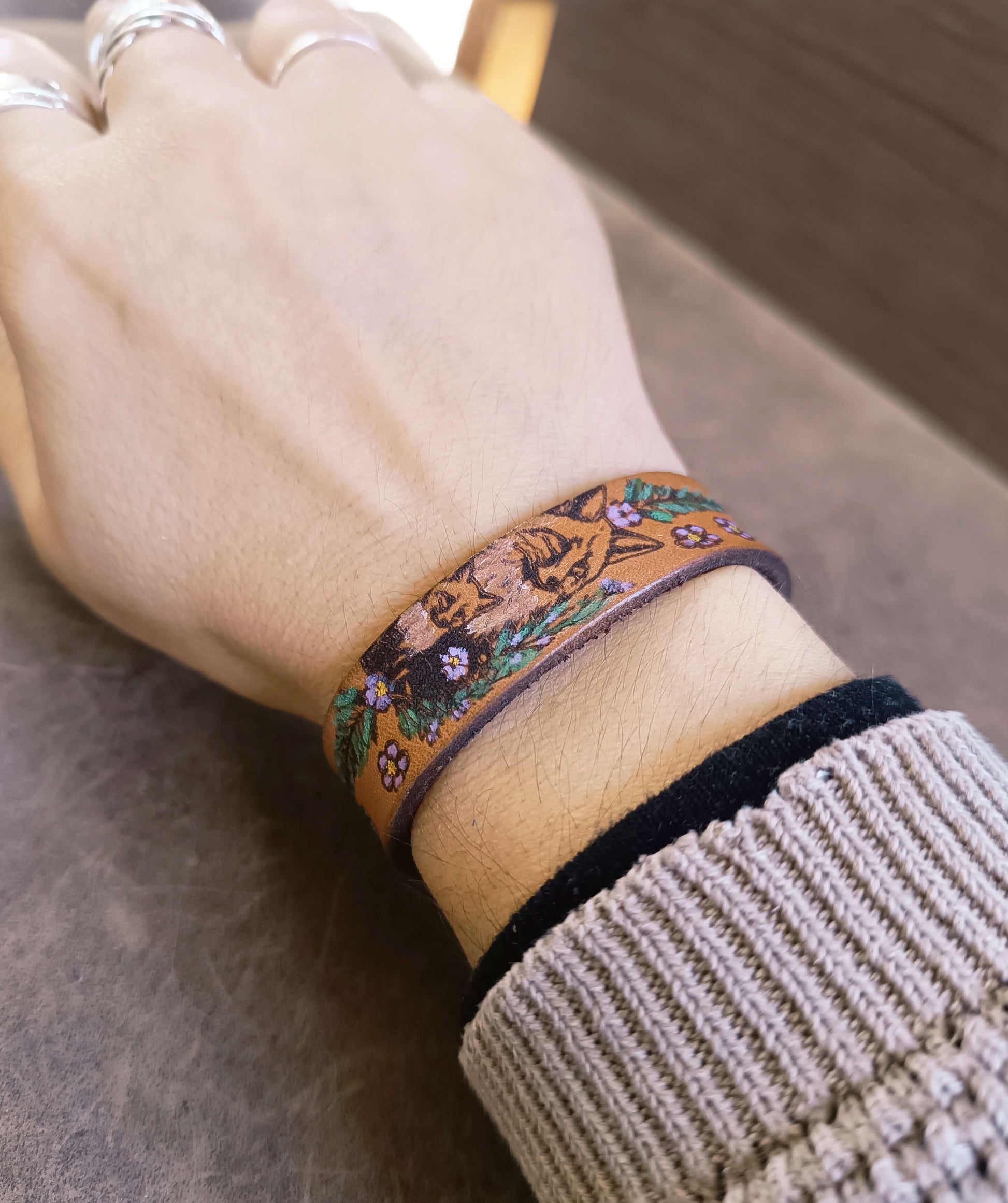Hand wearing a floral-patterned bracelet on a neutral background