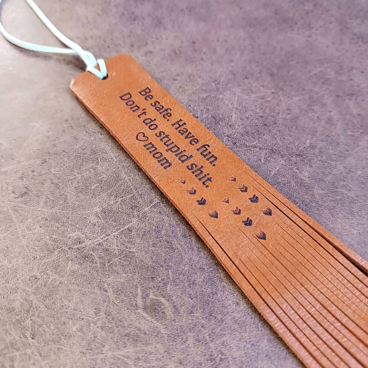 Brown leather bookmark with engraved text on a gray surface