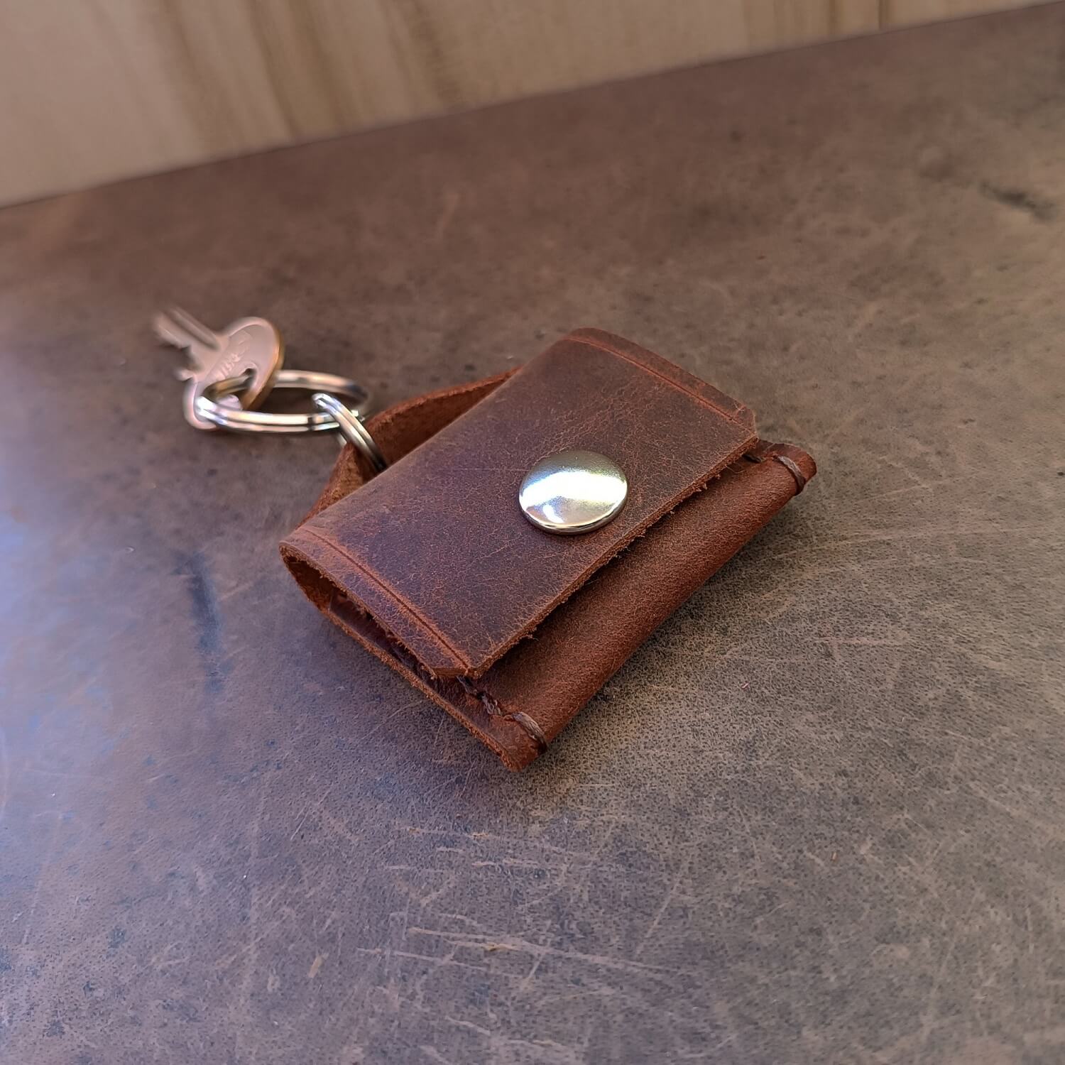 Chocolate Brown leather ringholder keychain with a silver snap button on a textured surface and clipped on keys