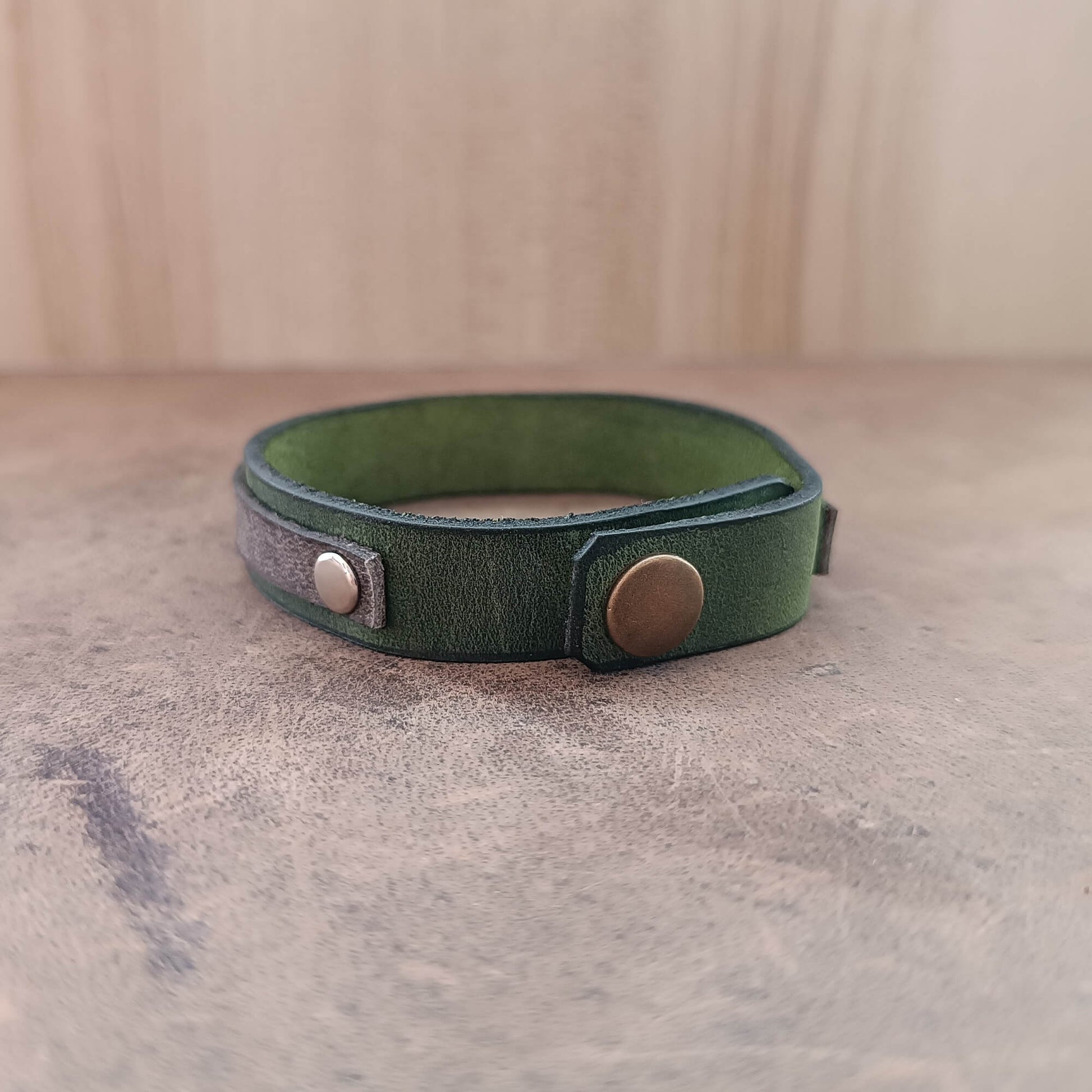 Green leather bracelet with metal clasps on a textured surface back view