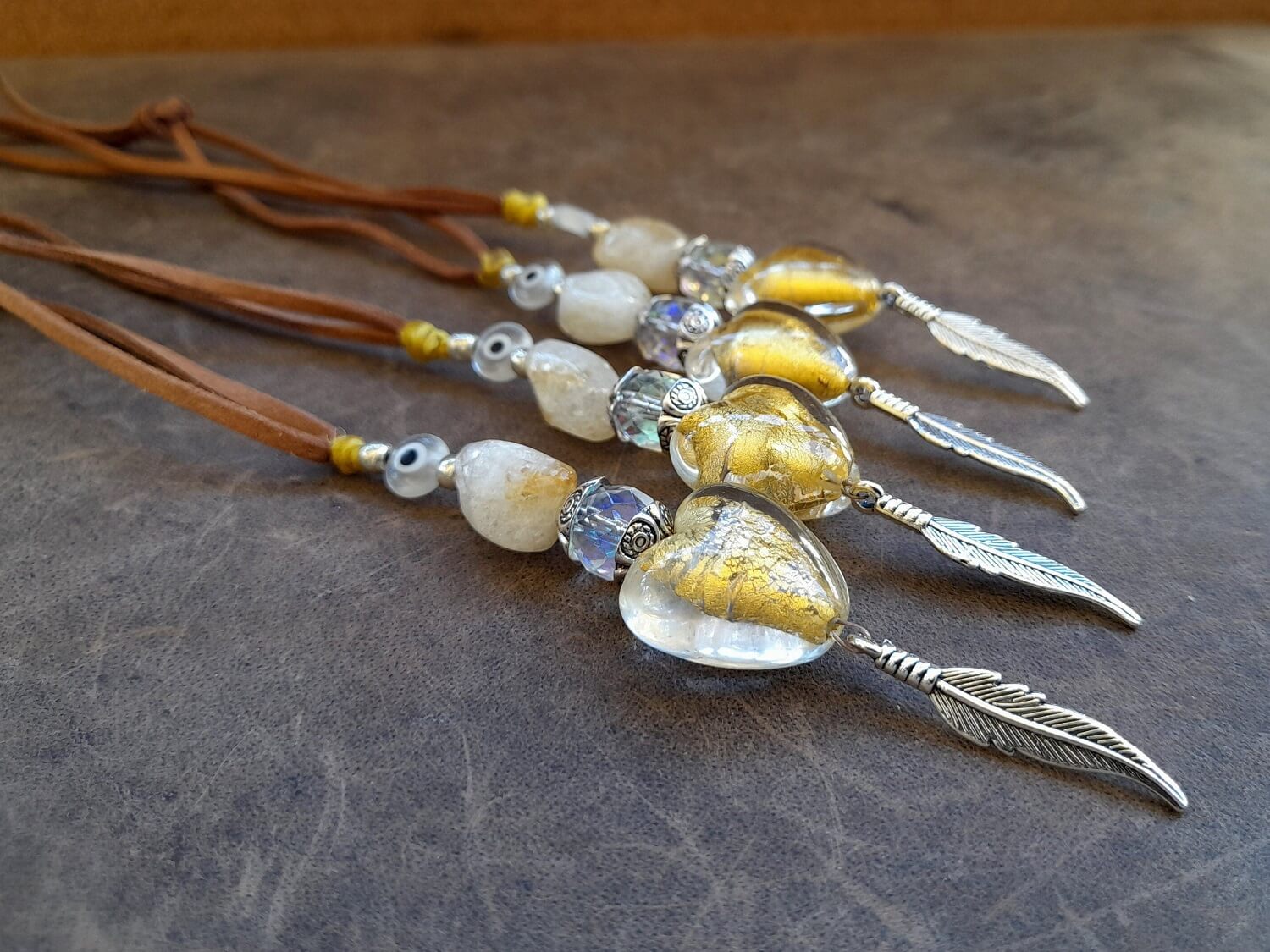 A series of boho-style car charms with natural citrine stones, yellow crystal hearts, and silver feathers, attached to brown suede cords.