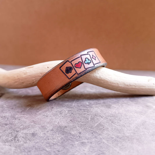 Leather bracelet with card suit symbols on a wooden surface