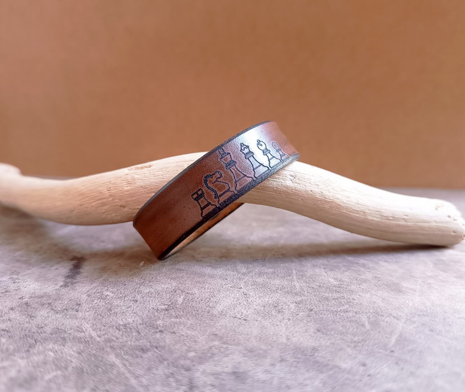 Brown leather bracelet with engraved design on a wooden stick against a beige background