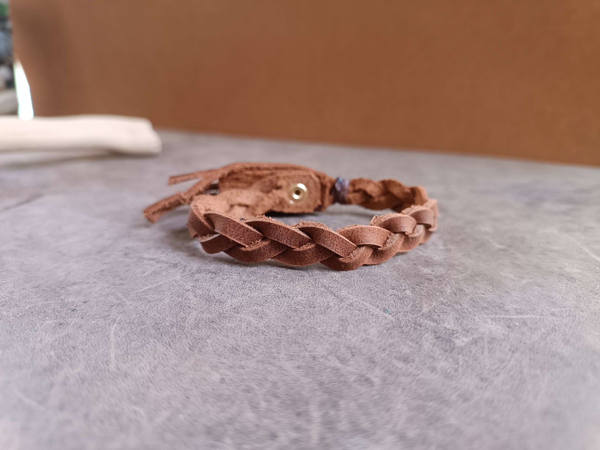 Brown braided leather bracelet on a gray surface with a blurred brown background