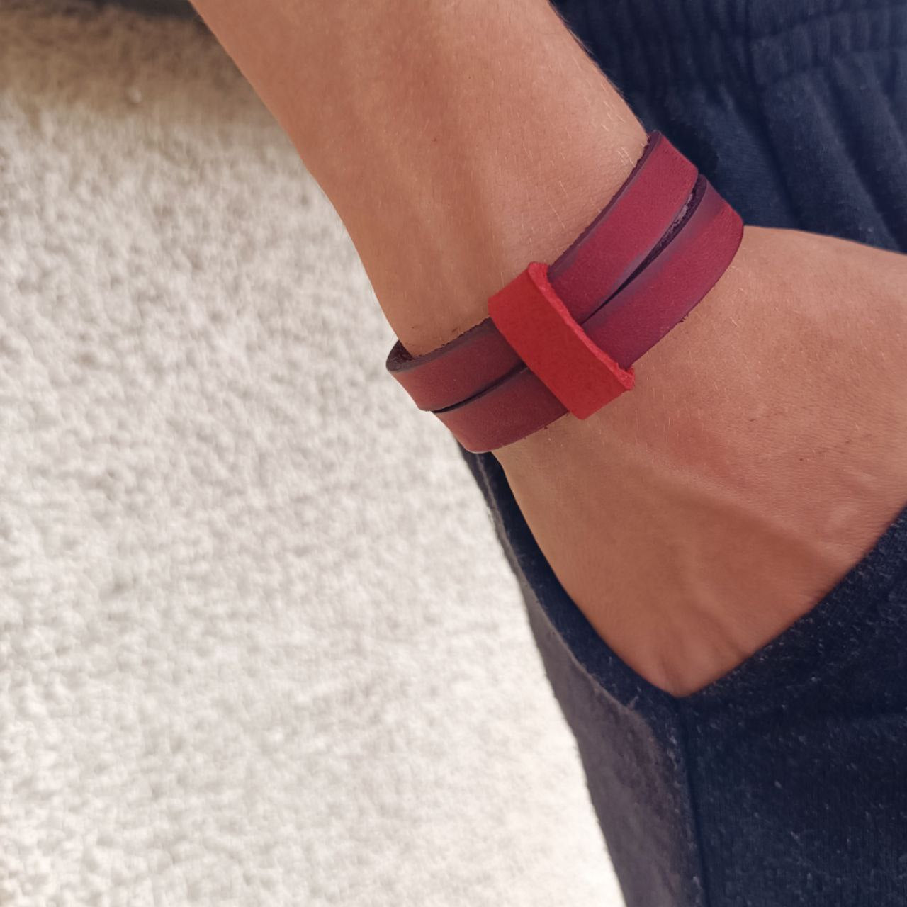 A man's wrist wearing a dark red leather cuff bracelet with a choker collar style and a matching loop.