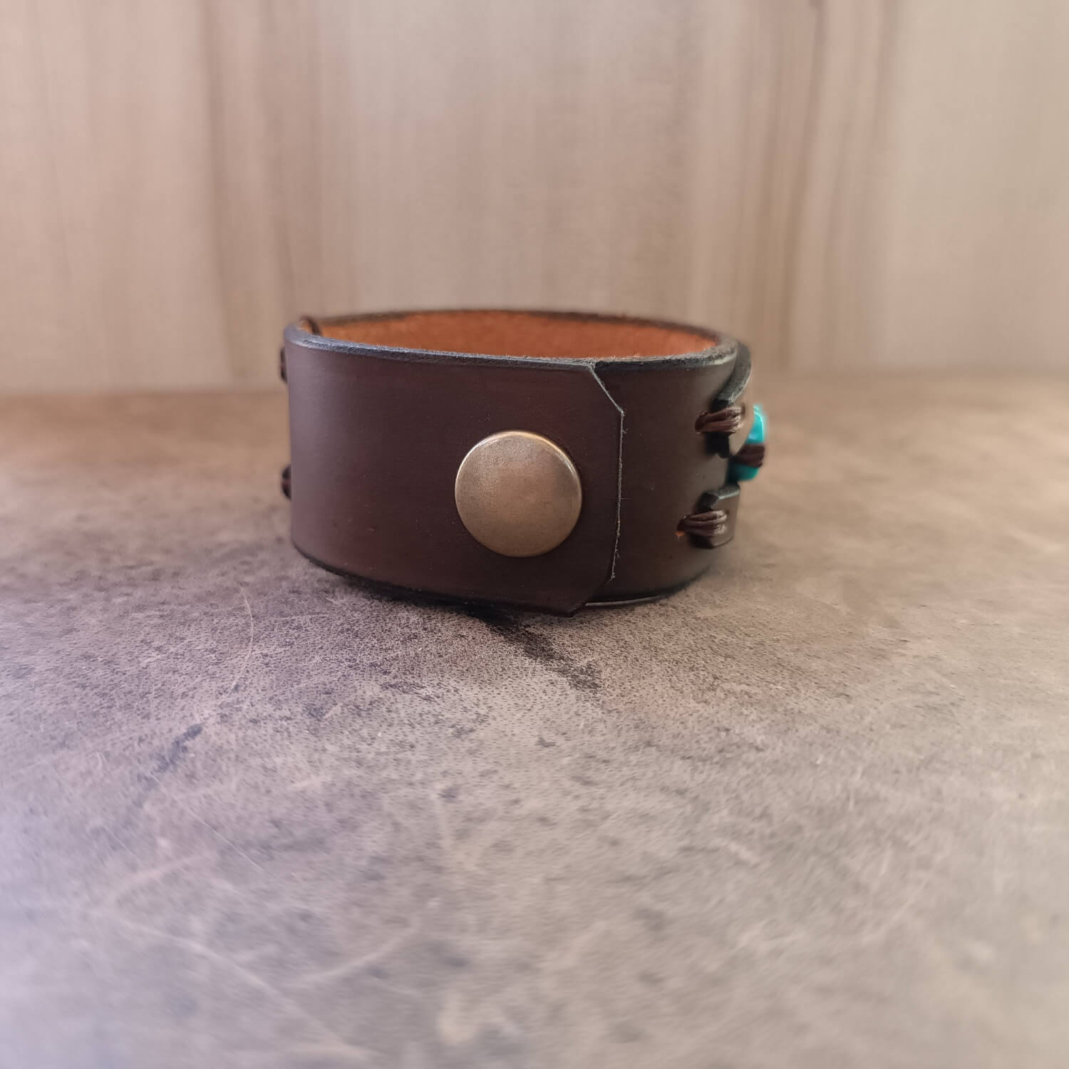 Brown leather bracelet with a metal button on a textured surface