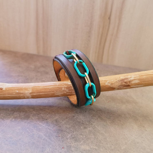 Brown leather bracelet with turquoise chain links on a wooden stick against a wooden background