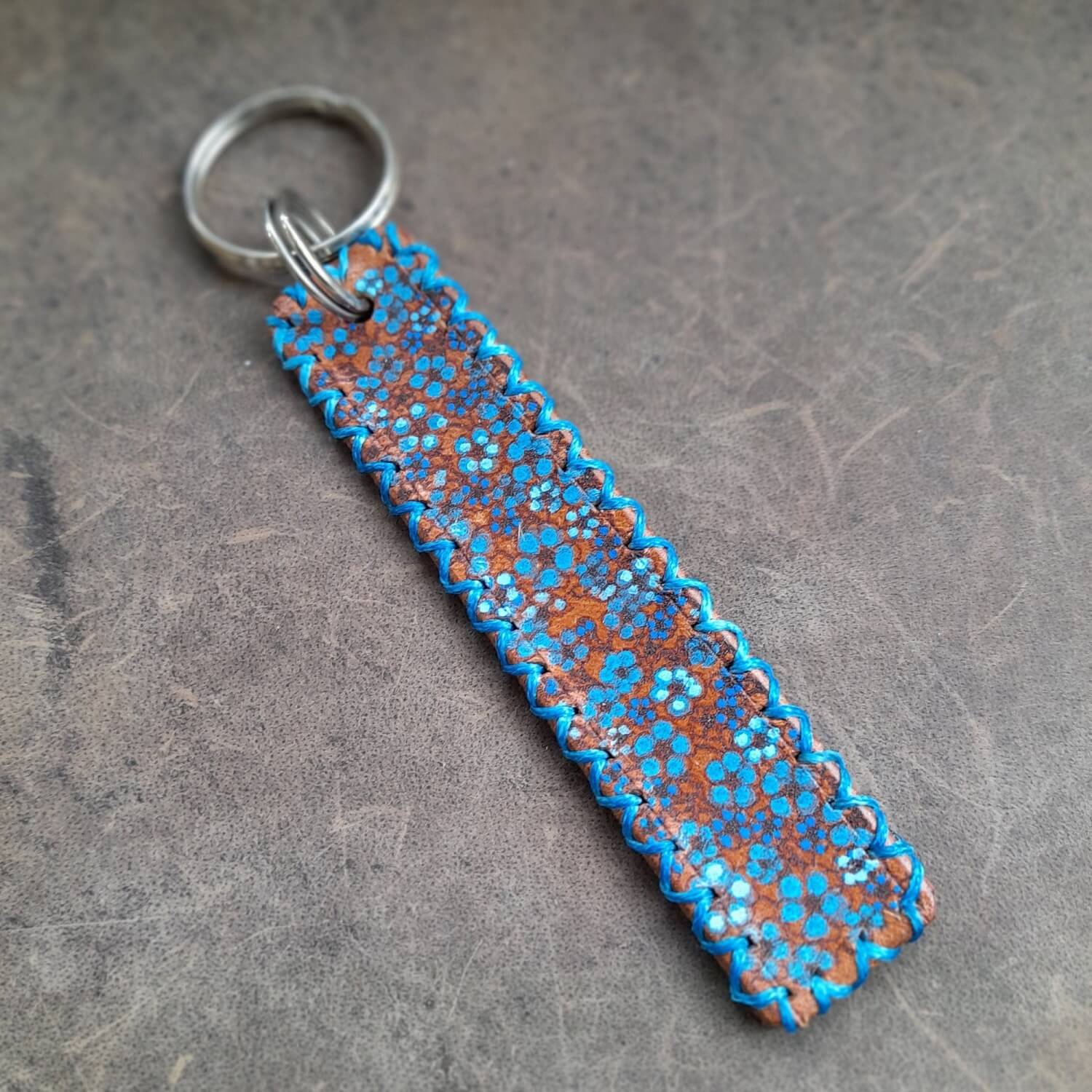 Detailed close-up of the hand-painted forget-me-not flowers on the keychain, showing the vibrant colors, laser-engraved texture, and blue beeswax thread stitching.
