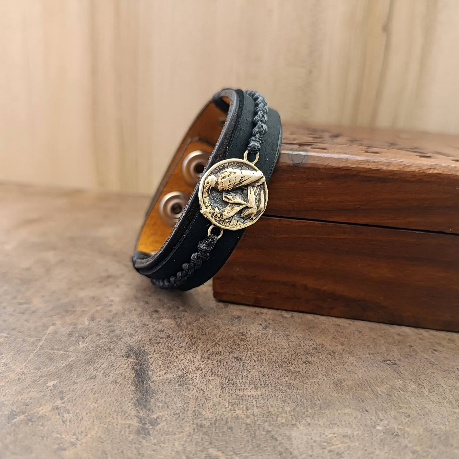close up side view of the black brown braided leather raven bracelet resting on an antique ooden jewelry box