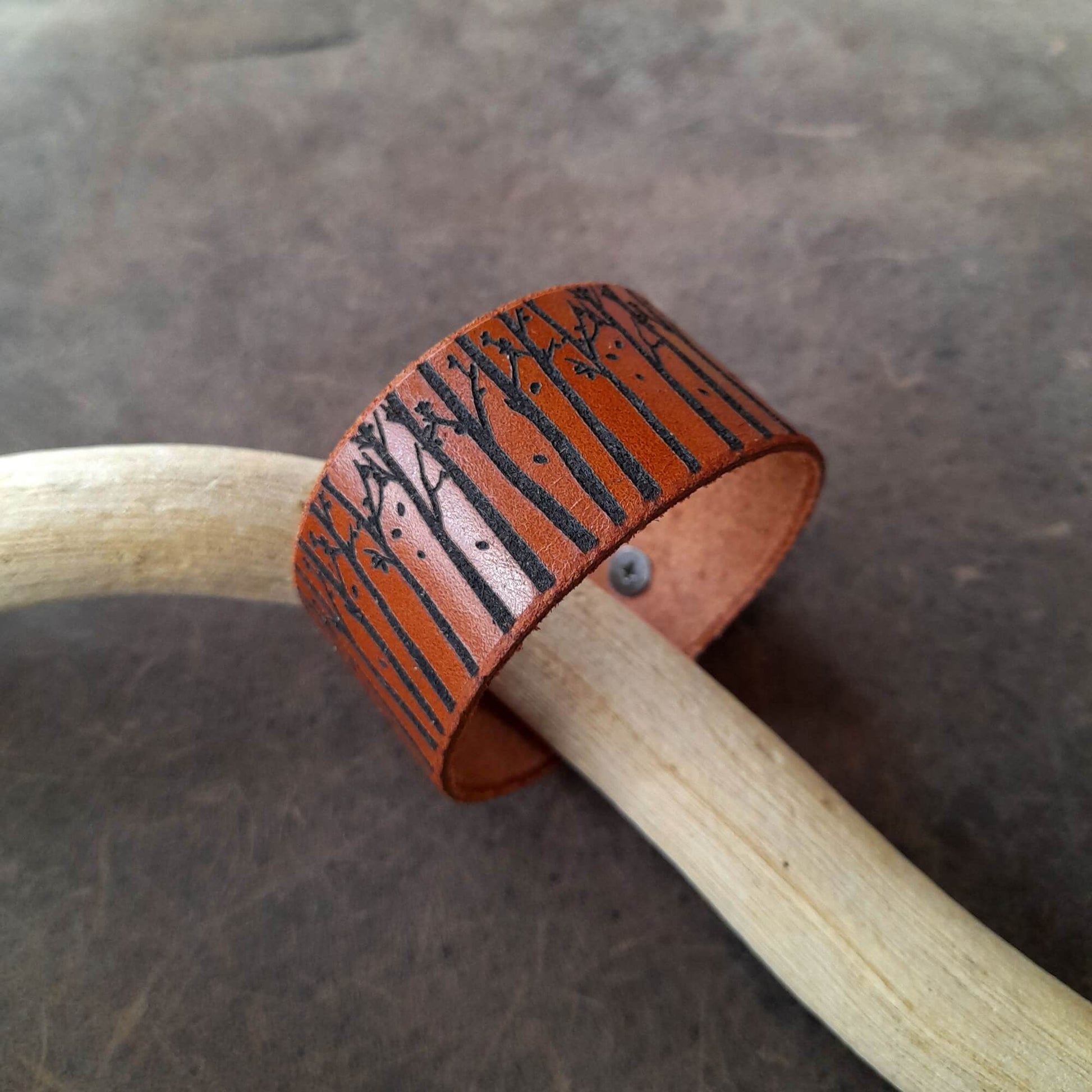 Brown leather cuff with tree pattern on a wooden stick against a dark background