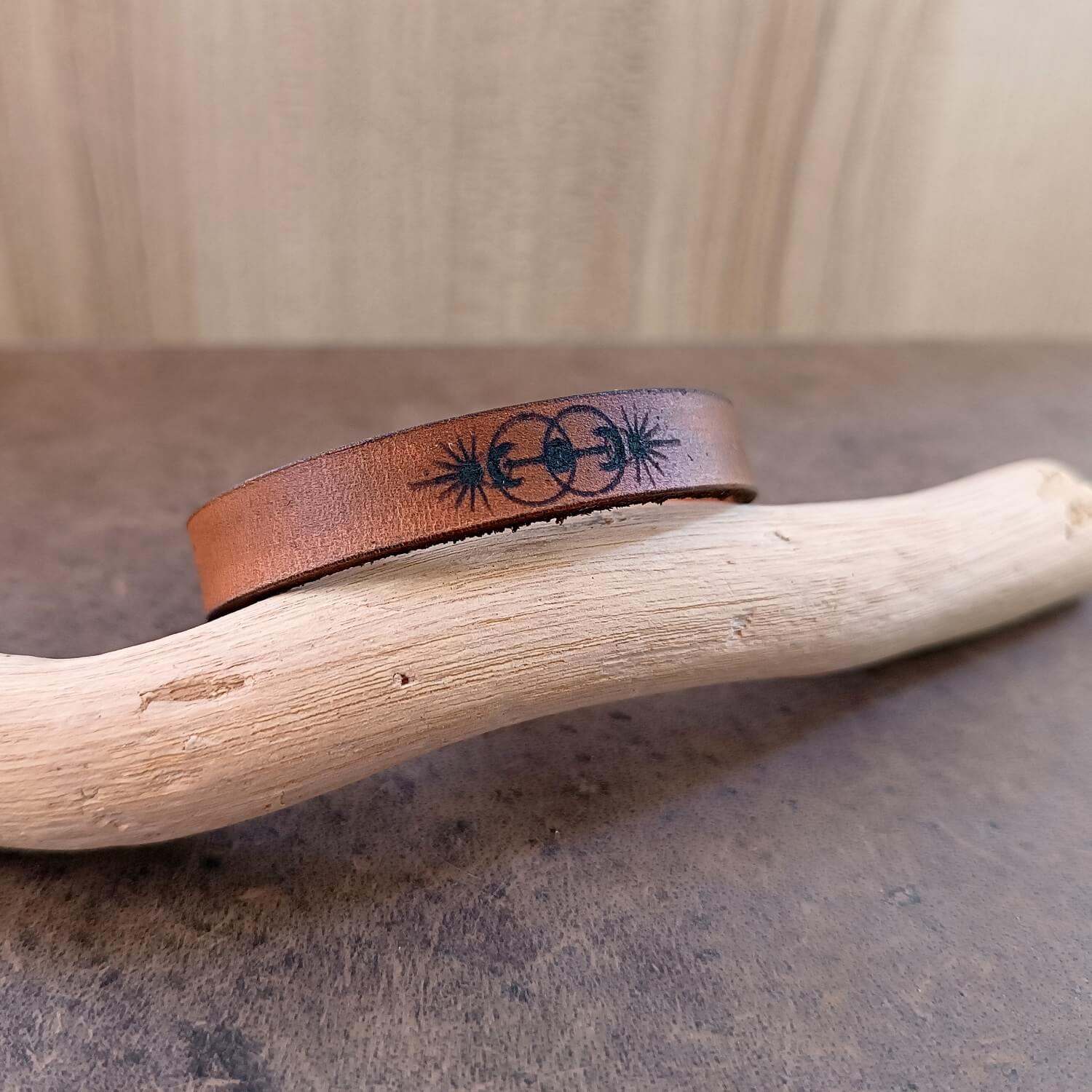 Brown leather bracelet with a black vesica piscis design on a wooden branch