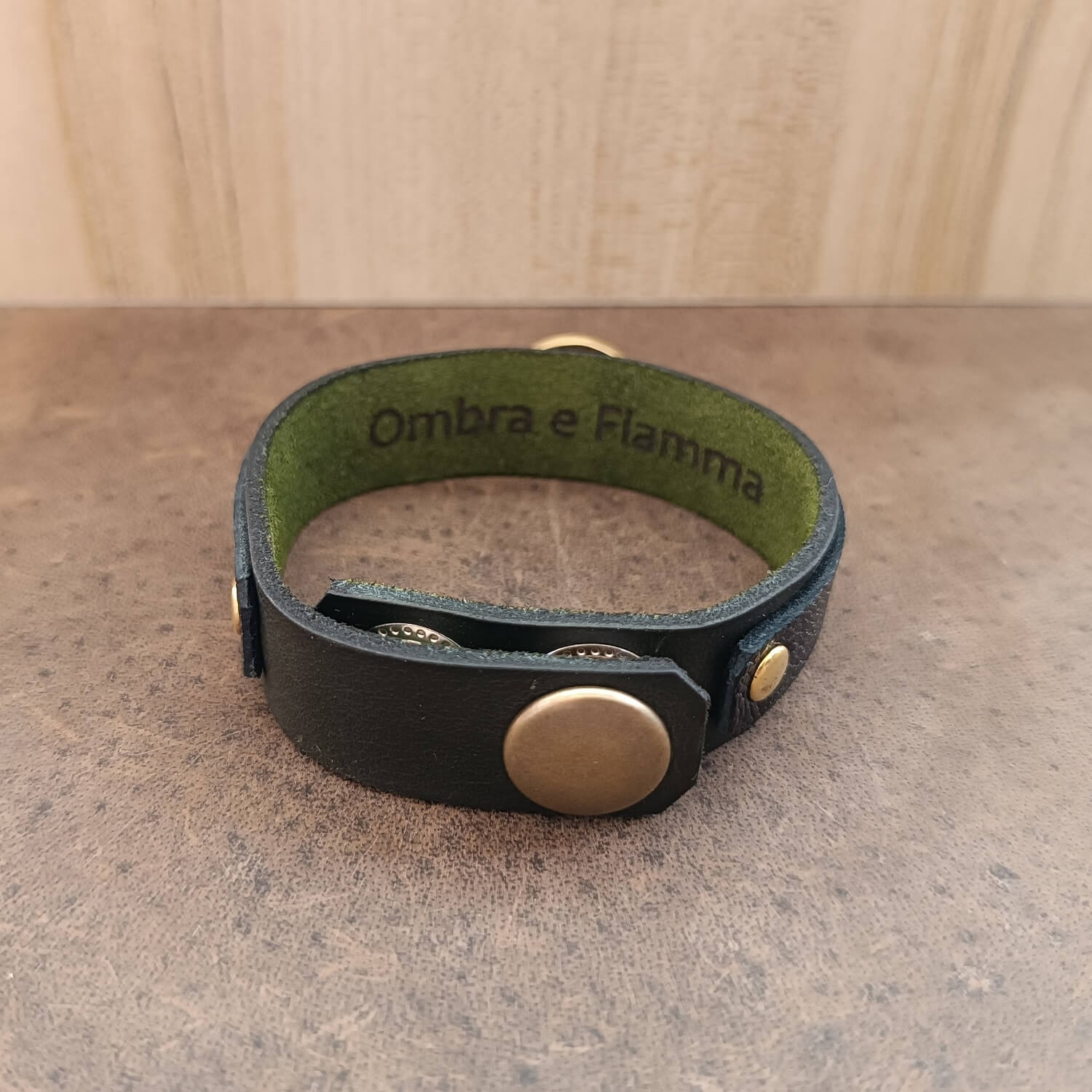 Backside close-up of the Vincenzo Bracelet Cobra Edition revealing the antique bronze snap closure—its solid click a promise in itself. The underside of the bracelet features the subtle engraving “Ombra e Fiamma” (“Shadow and Flame”) etched into grapevine-green leather, a quiet testament to legacy, pain, and power carried in silence.