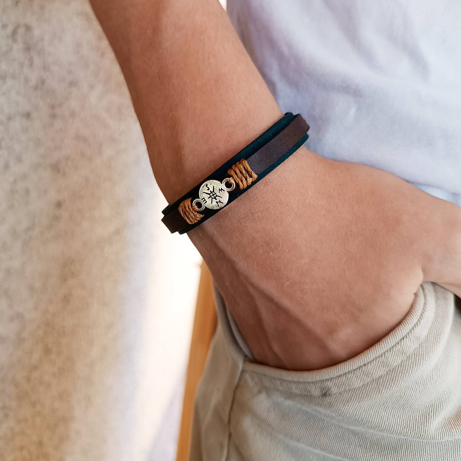 Close-up of a wrist wearing a brown leather bracelet with a compass charm.
