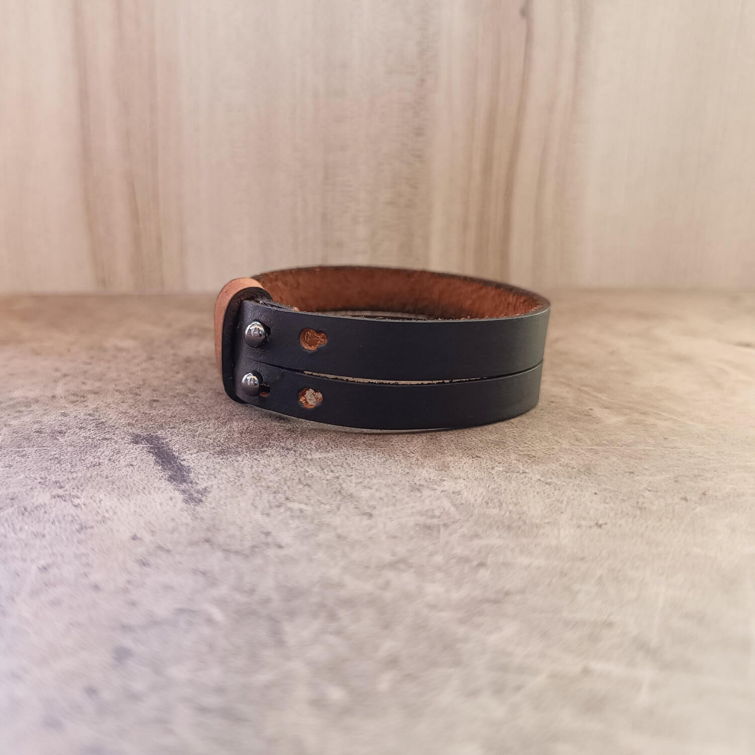 Black leather bracelet with brown interior on a textured surface