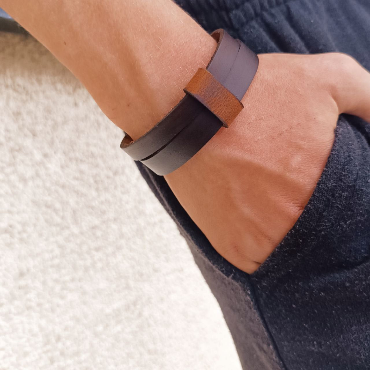 A person wearing a dark brown leather cuff bracelet with a choker collar style.