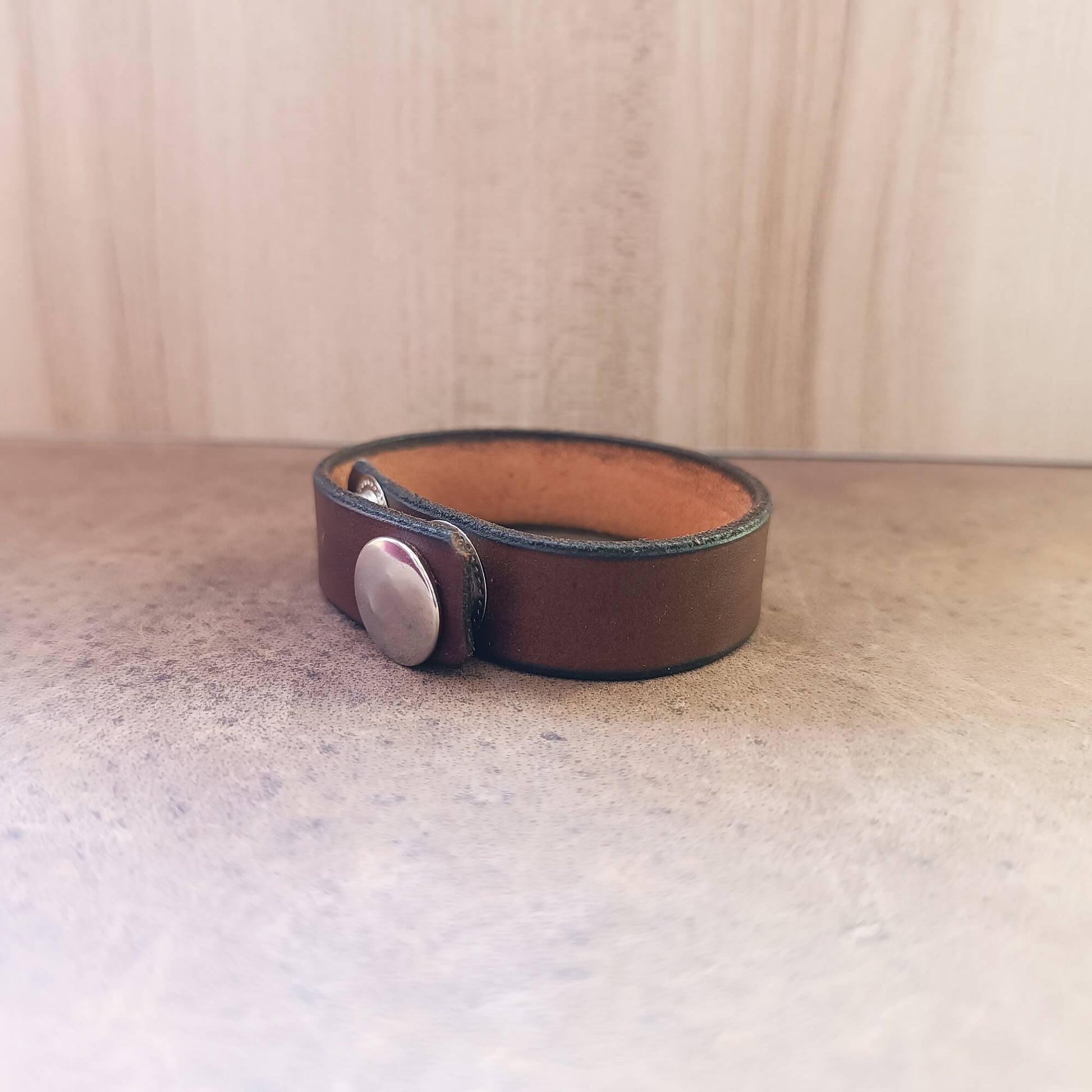Brown leather bracelet with a silver button on a light wooden surface