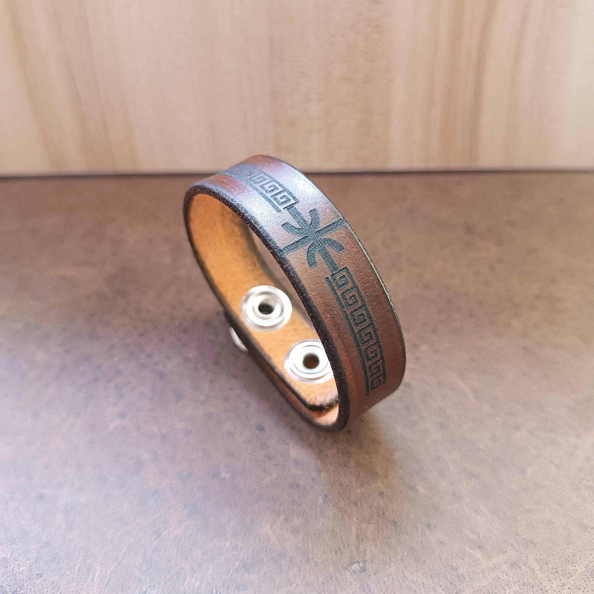 Brown leather bracelet with delphic epsilon and meander design on a wooden surface