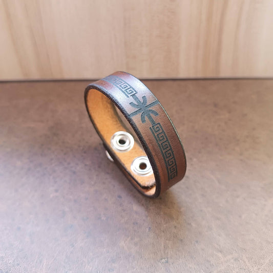 Brown leather bracelet with delphic epsilon and meander design on a wooden surface