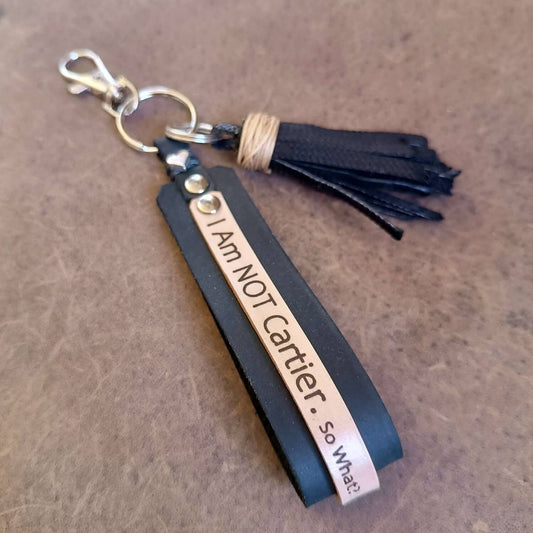 Black leather keychain with tassel and engraved text on a brown surface