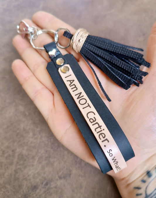 Black keychain with tassel and engraved text held in a hand against a neutral background