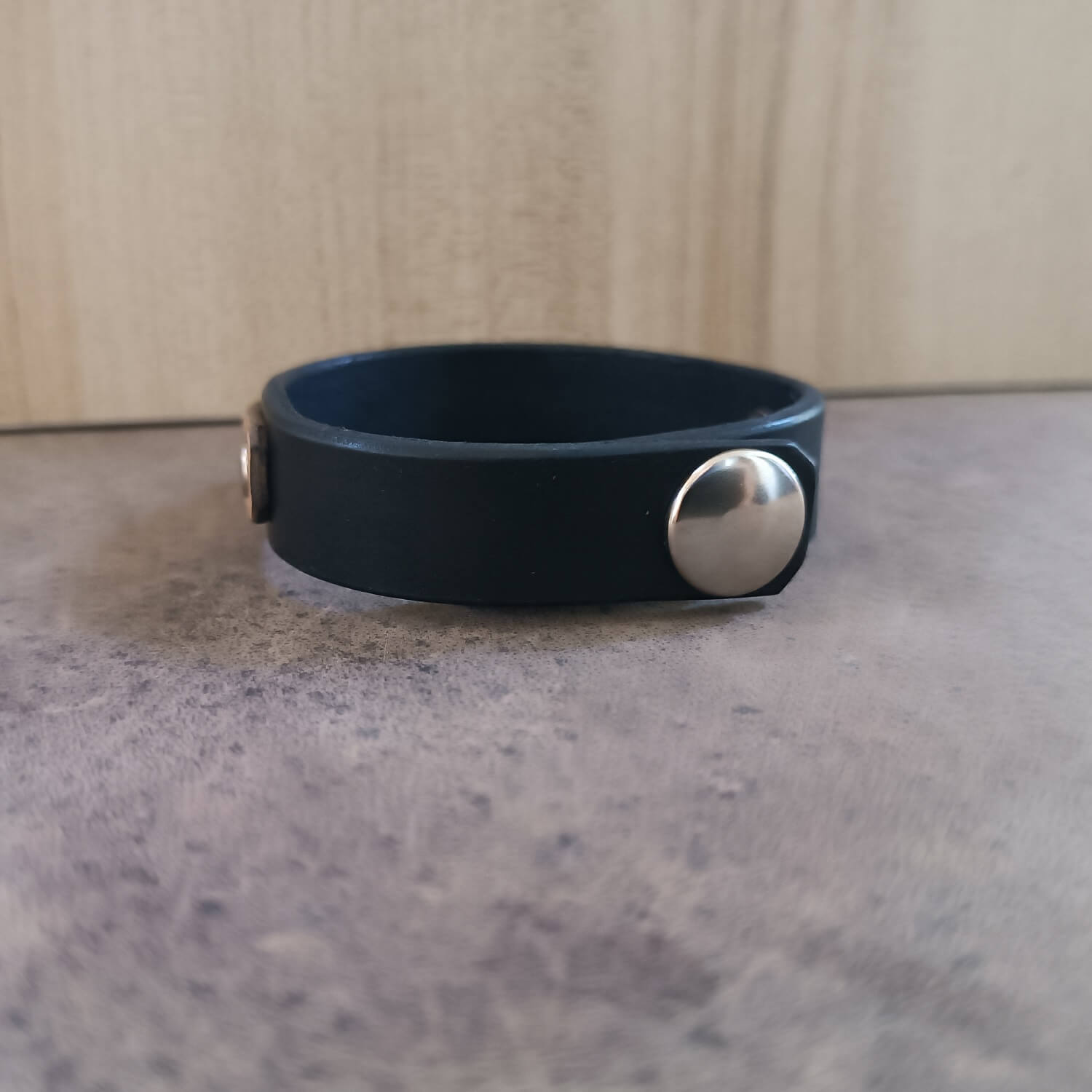 Double Helix Black leather bracelet with a silver button on a gray surface