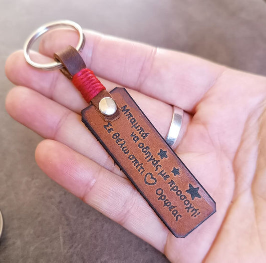 Brown leather keychain with text held in a hand against a neutral background