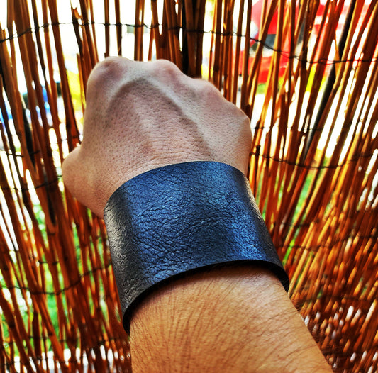 Hand wearing a black leather wristband against a woven background