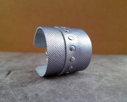 Silver textured cuff bracelet on a textured surface with a blurred background