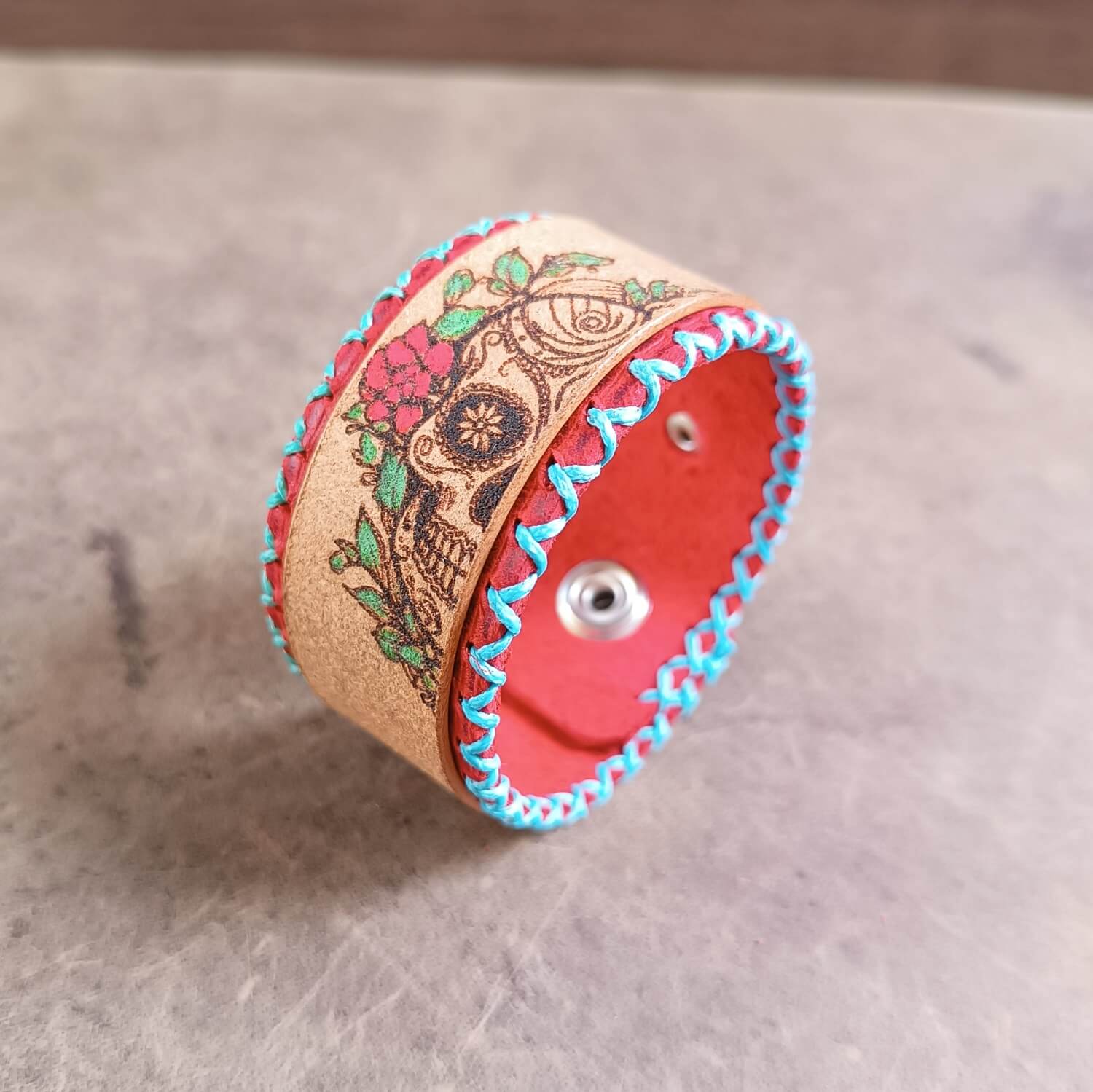 red floral sugar skull leather cuff, front view, showcasing light blue and turquoise stitching