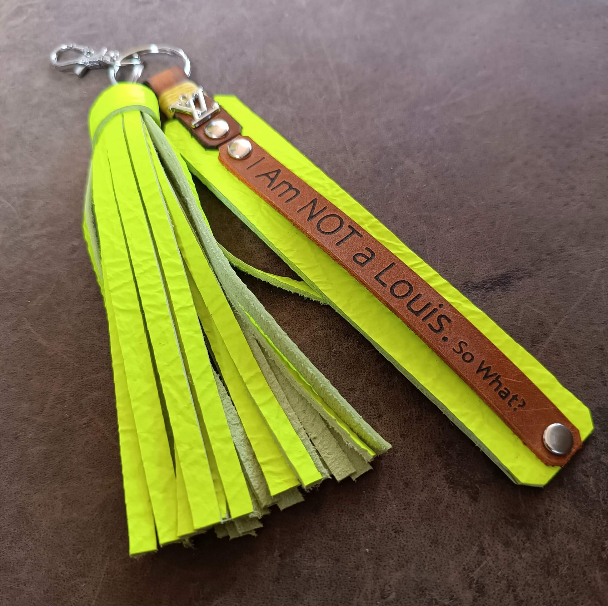 fluo yellow tassel keychain with brown leather tag on a brown background