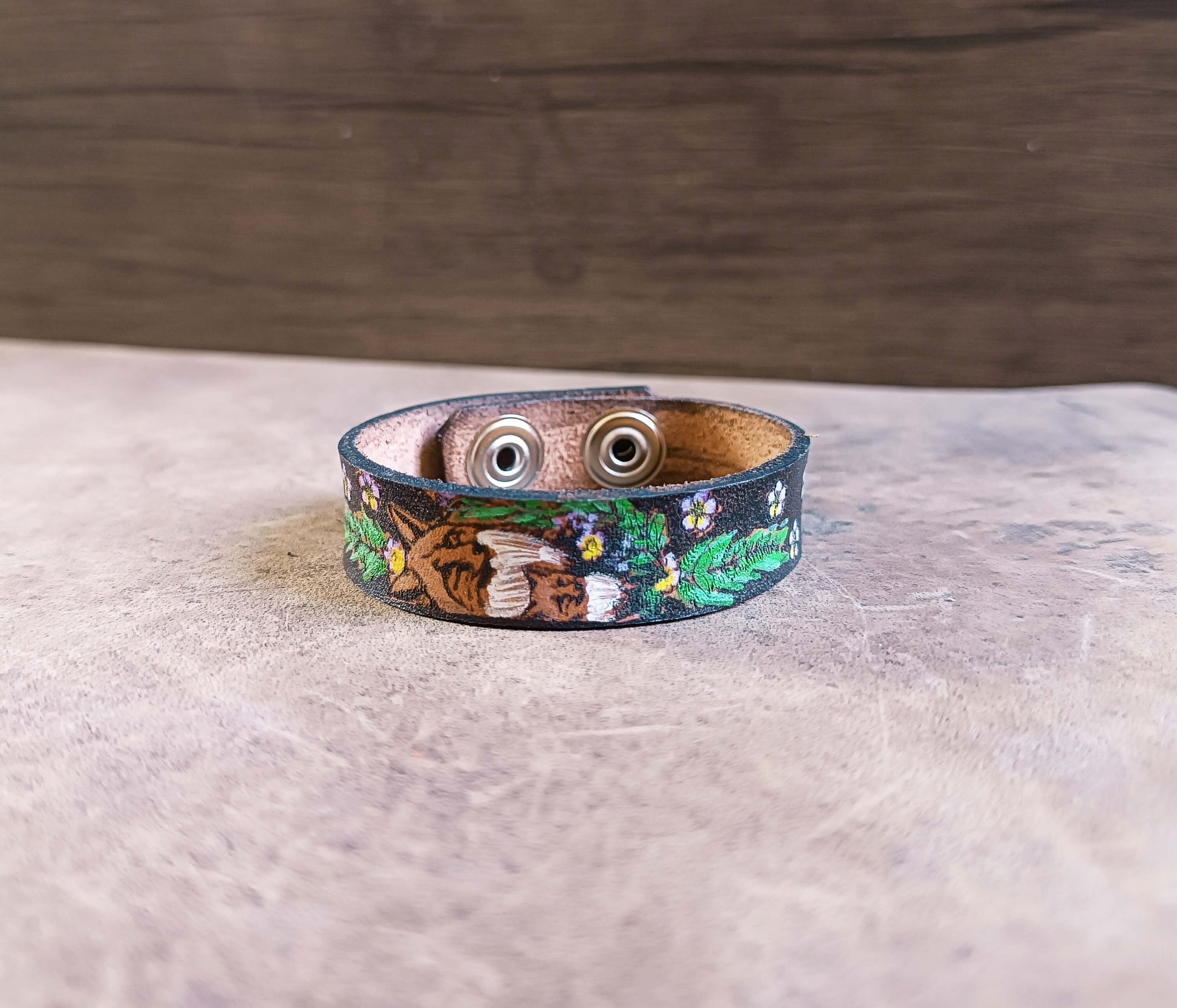 Leather bracelet with nature-themed design on a wooden surface