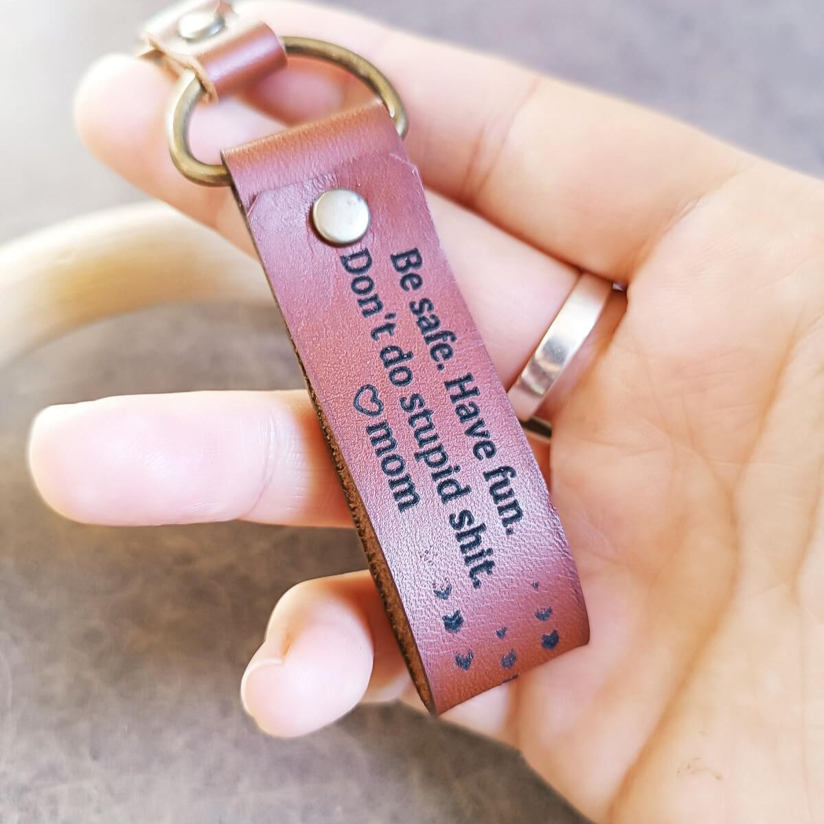 Brown leather keychain with engraved text held in a hand