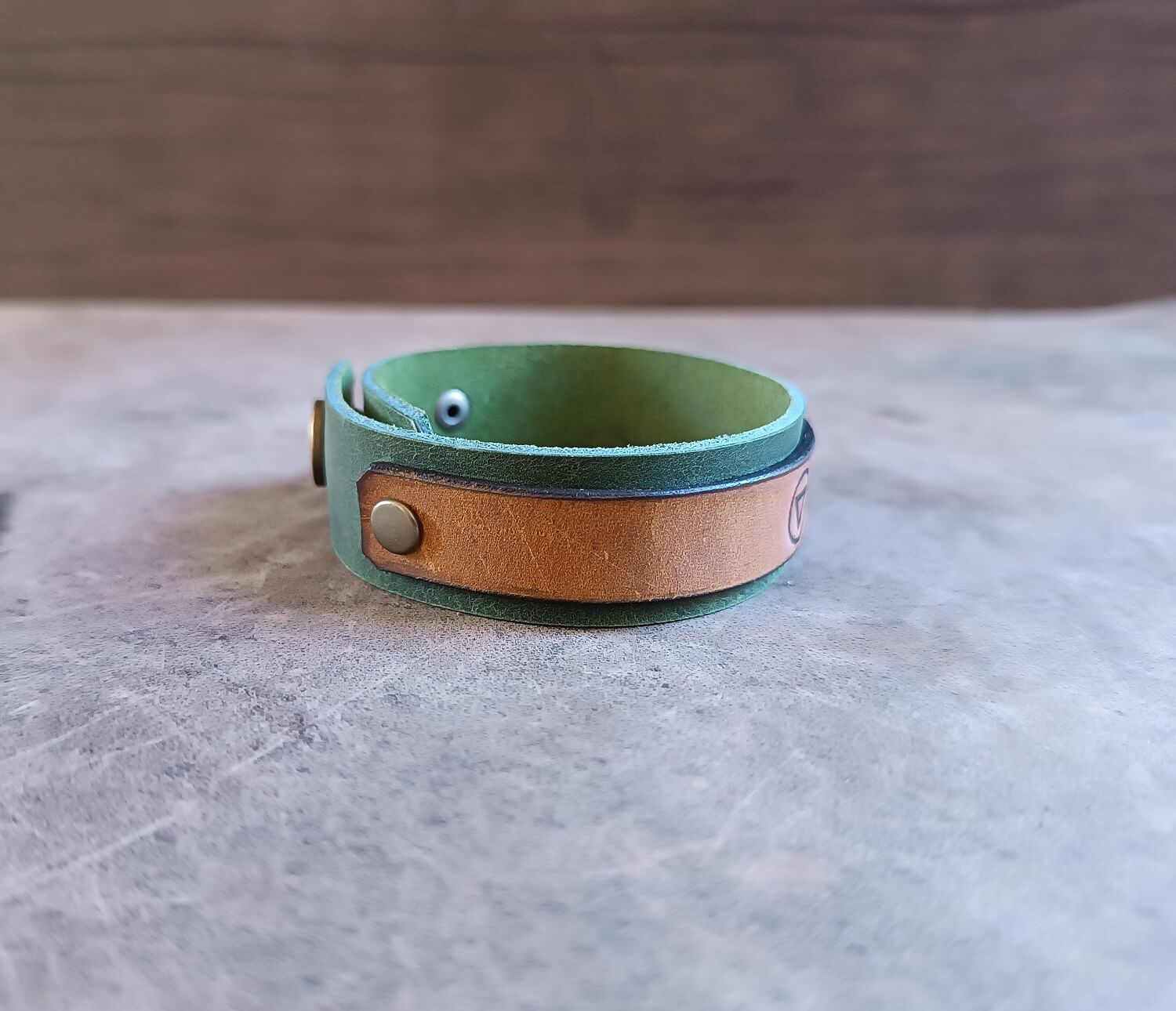 Green and brown leather bracelet on a gray surface with a wooden background