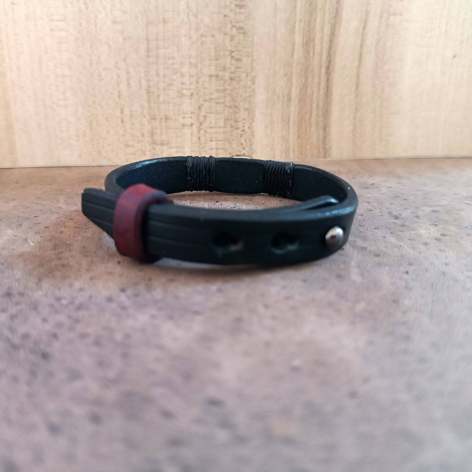 Black leather bracelet with a red accent on a wooden surface