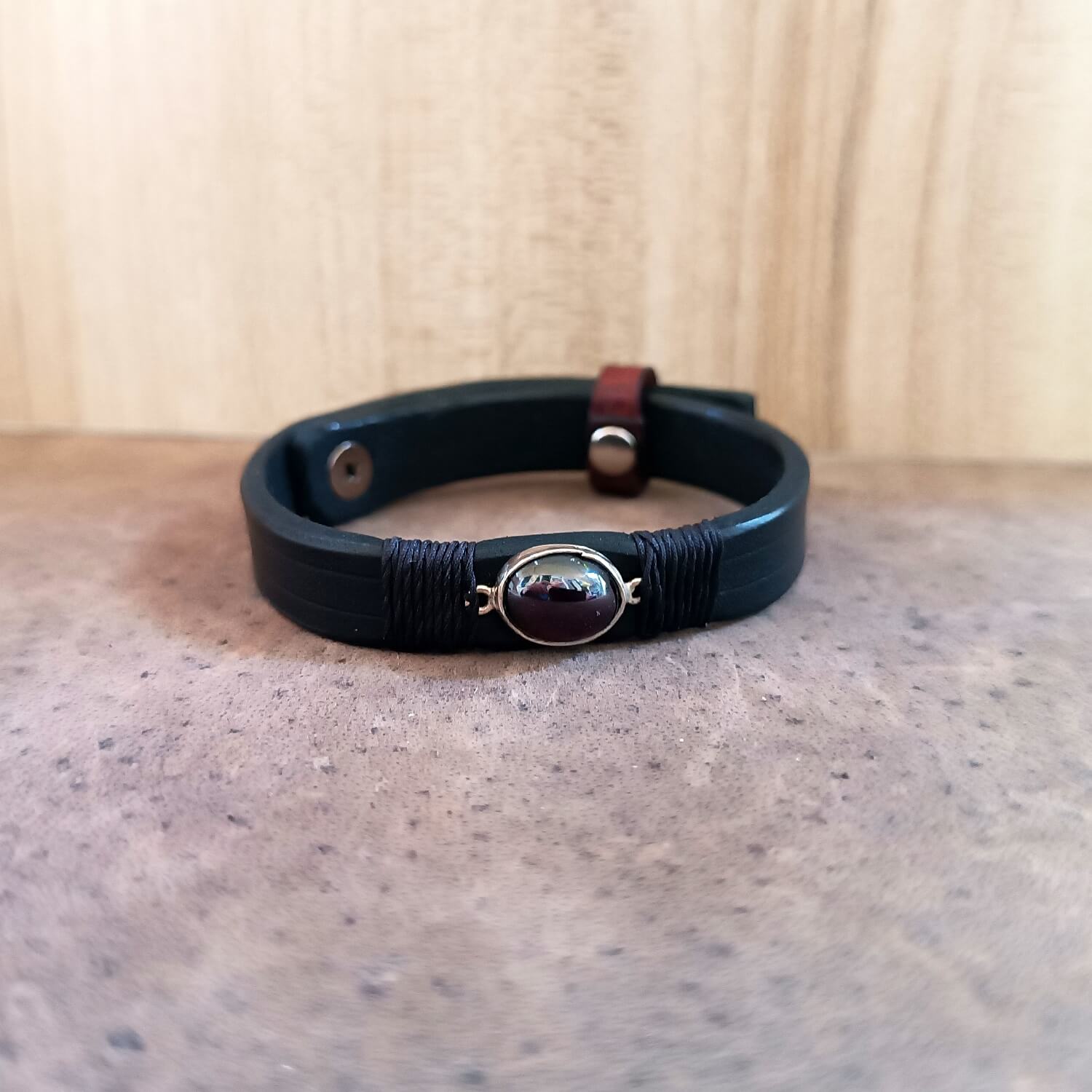 Black leather bracelet with a red garnet stone on a wooden surface
