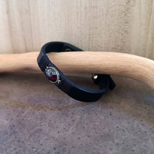 Black bracelet with a red garnet on a wooden surface