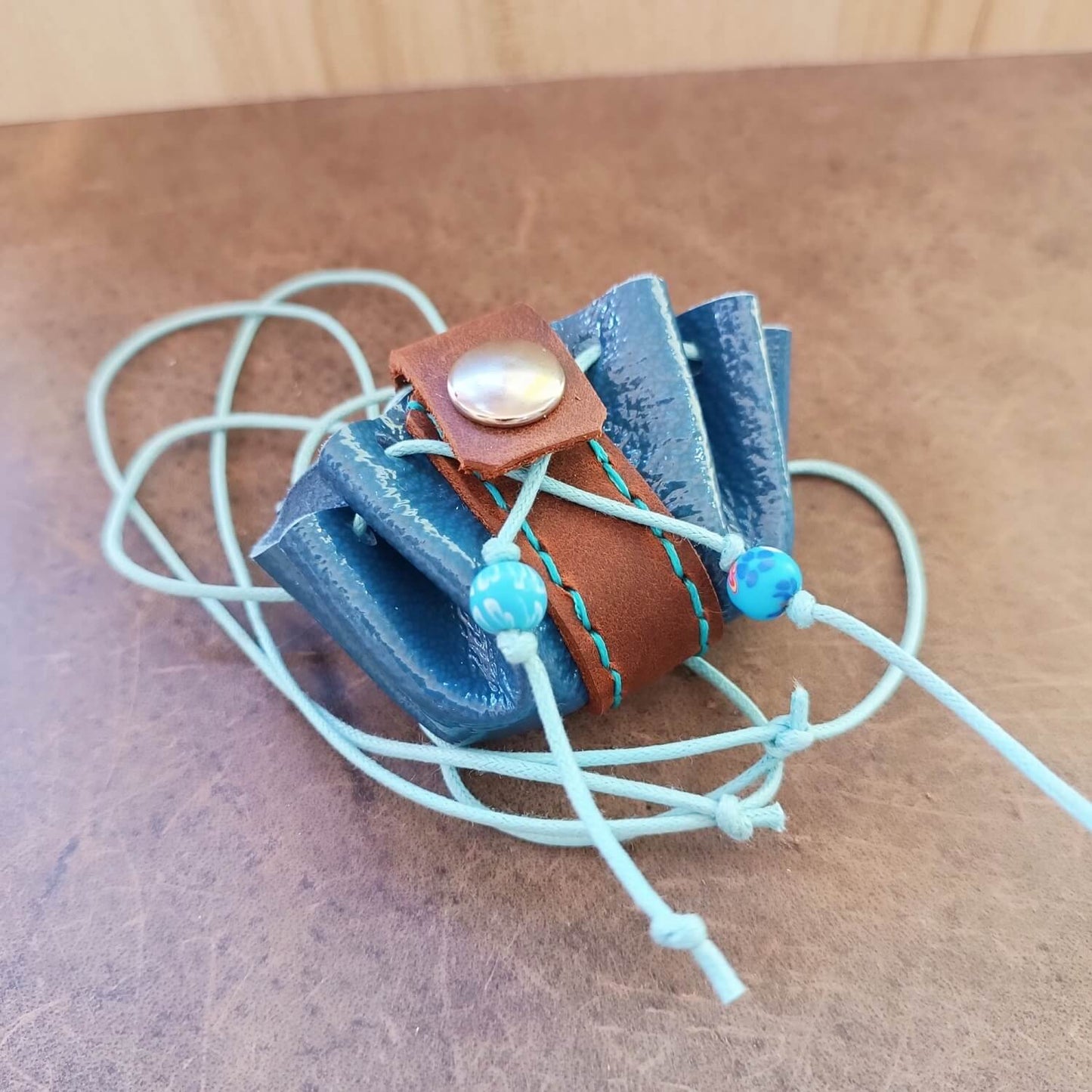 the glossy blue and brown leather neck pouch with its light adjusting cord, full view