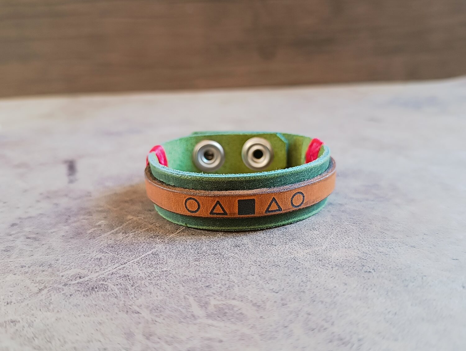 Green and brown leather bracelet with metal components on a textured surface