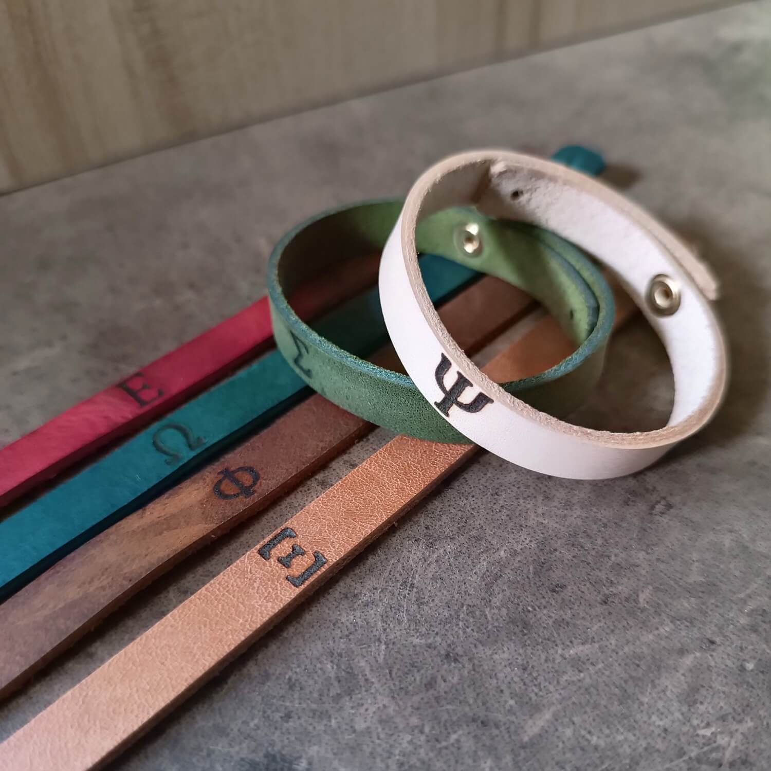 Group photo of Slim leather bracelets with engraved Greek letters, displayed flat and in all color variations.