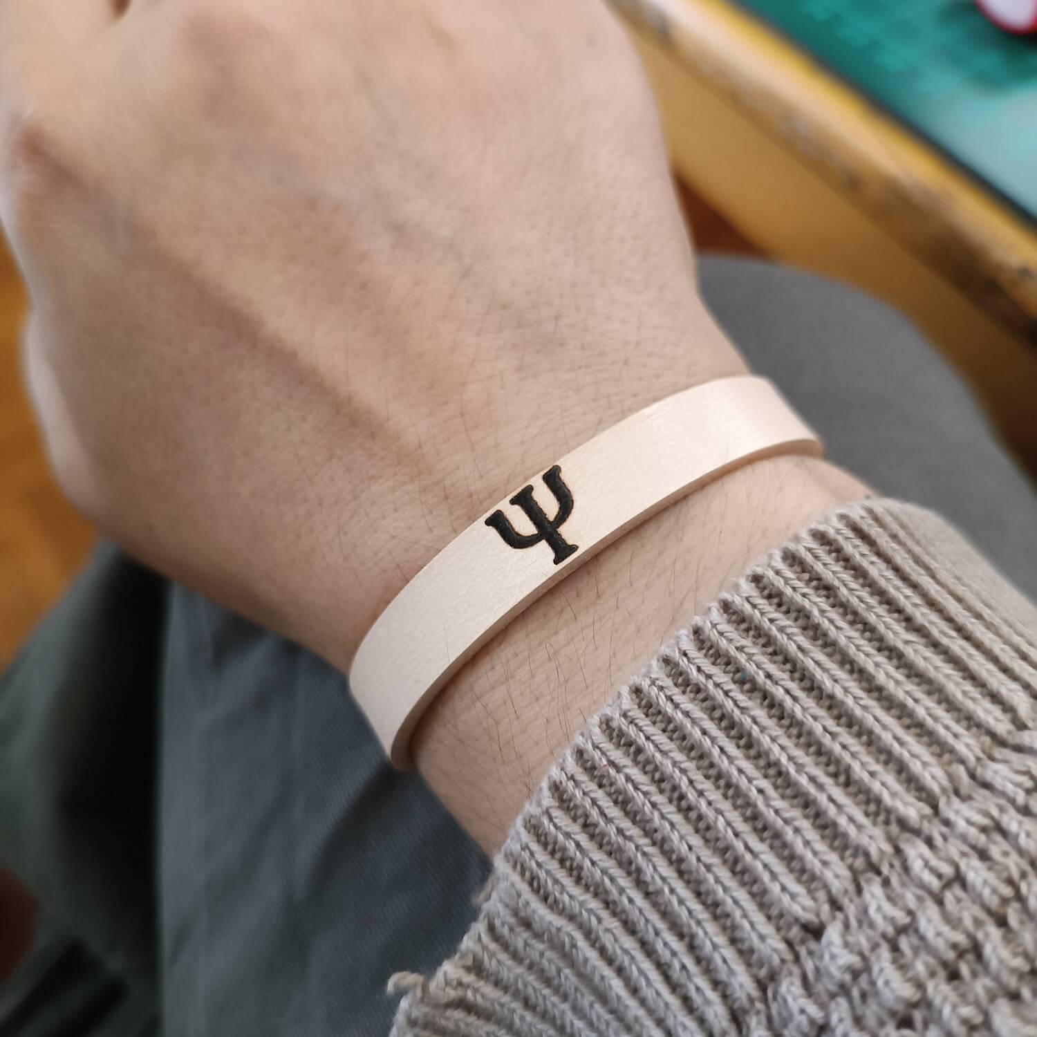 Minimalist unisex leather bracelet on wrist with visible Greek letter engraving