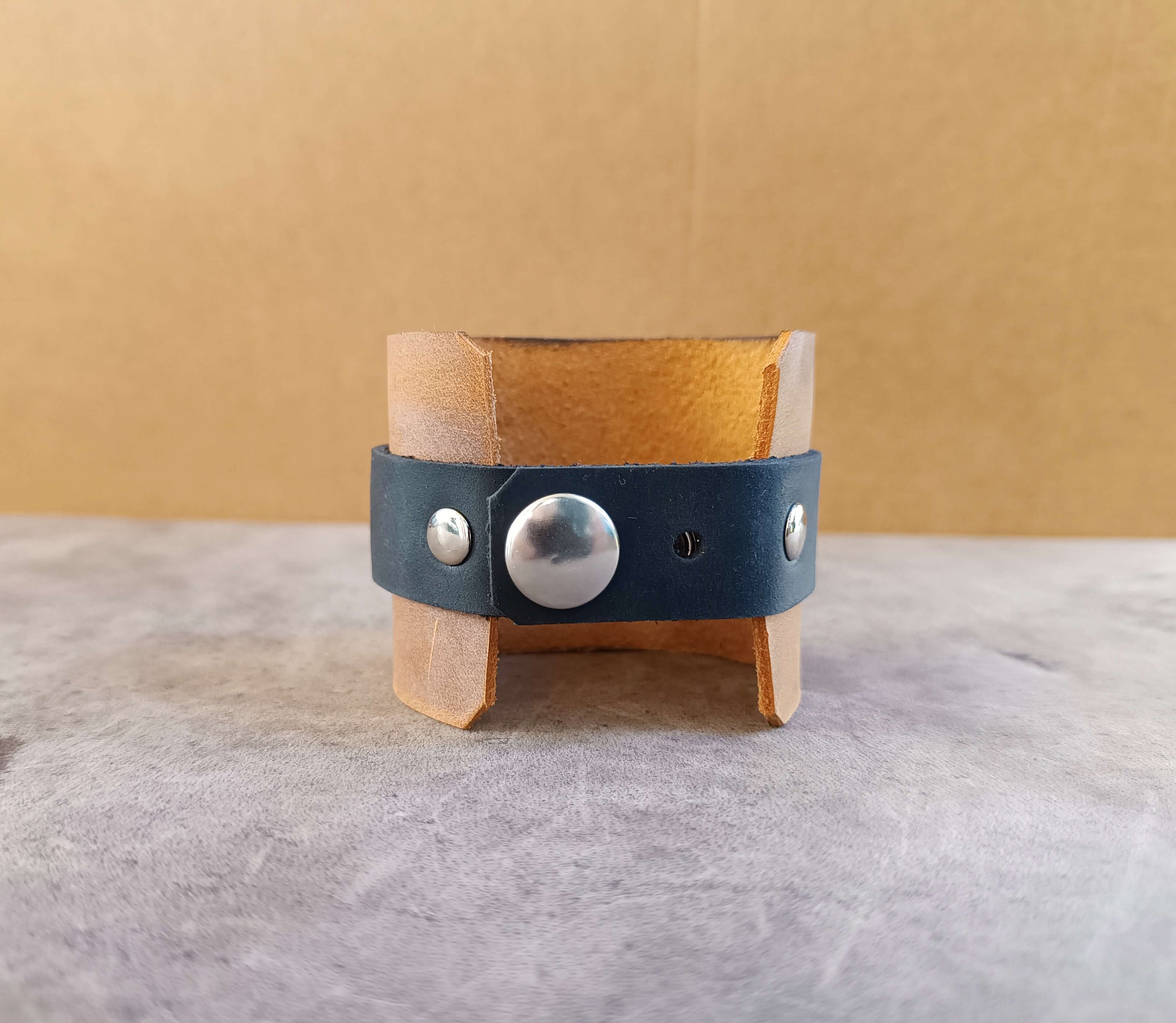 Leather bracelet with silver buttons on a stand against a beige background