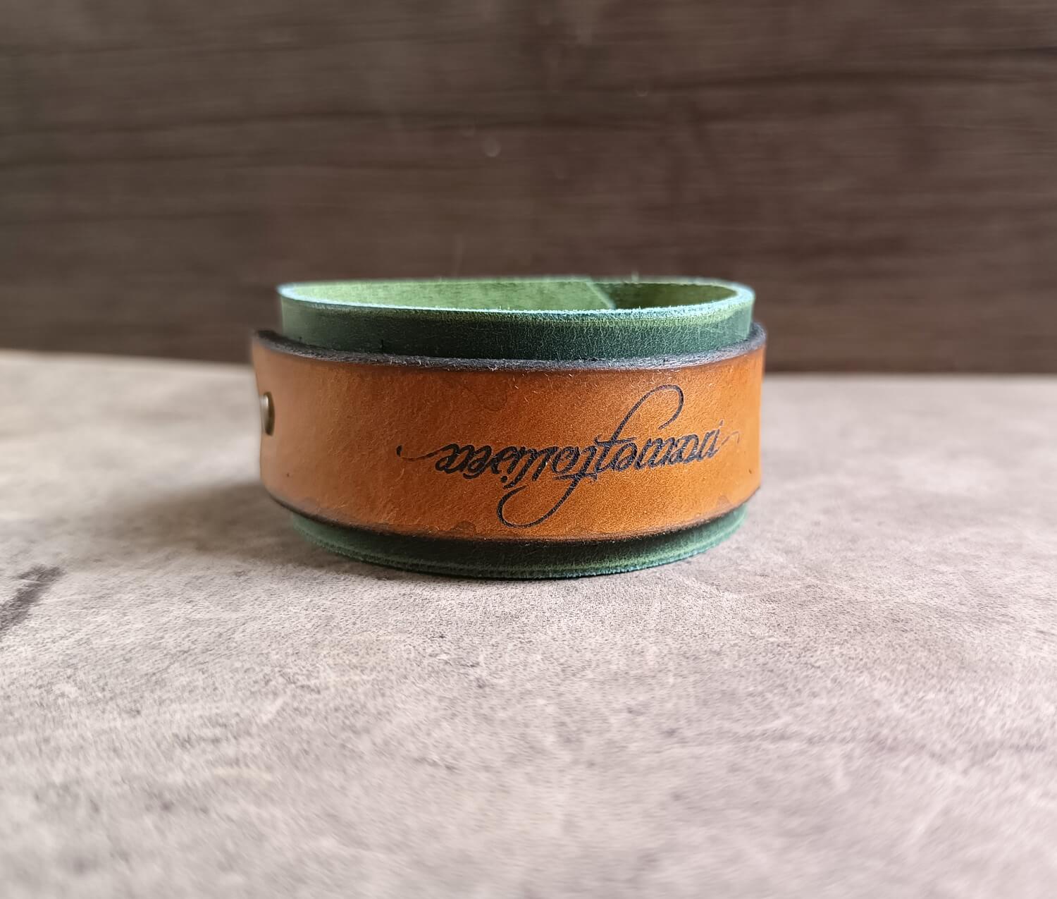 Leather wristband with green interior and brown exterior on a neutral background