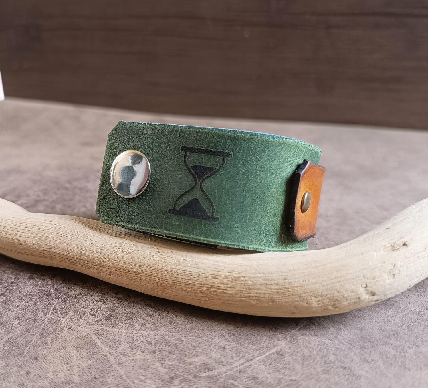 Green leather bracelet with hourglass design on a wooden stick