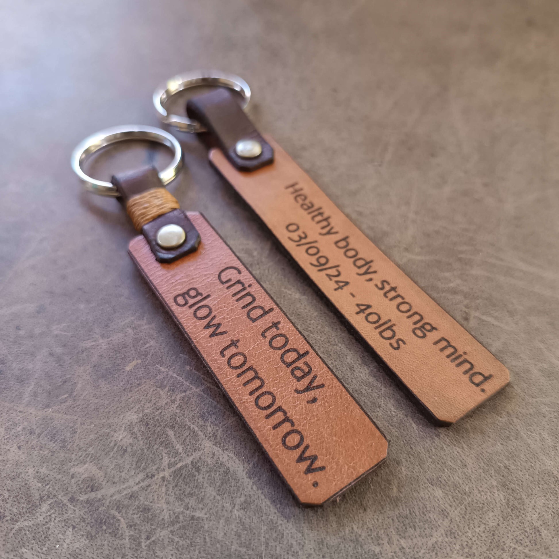 Two brown leather keychains with engraved text on a textured surface