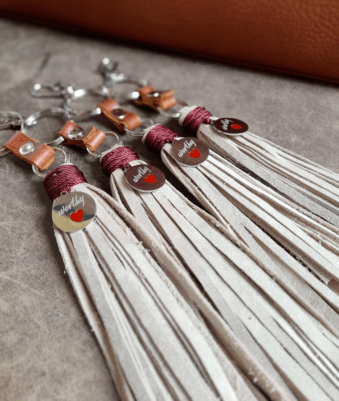Tassel keychains with leather accents and silver pendants on a textured surface