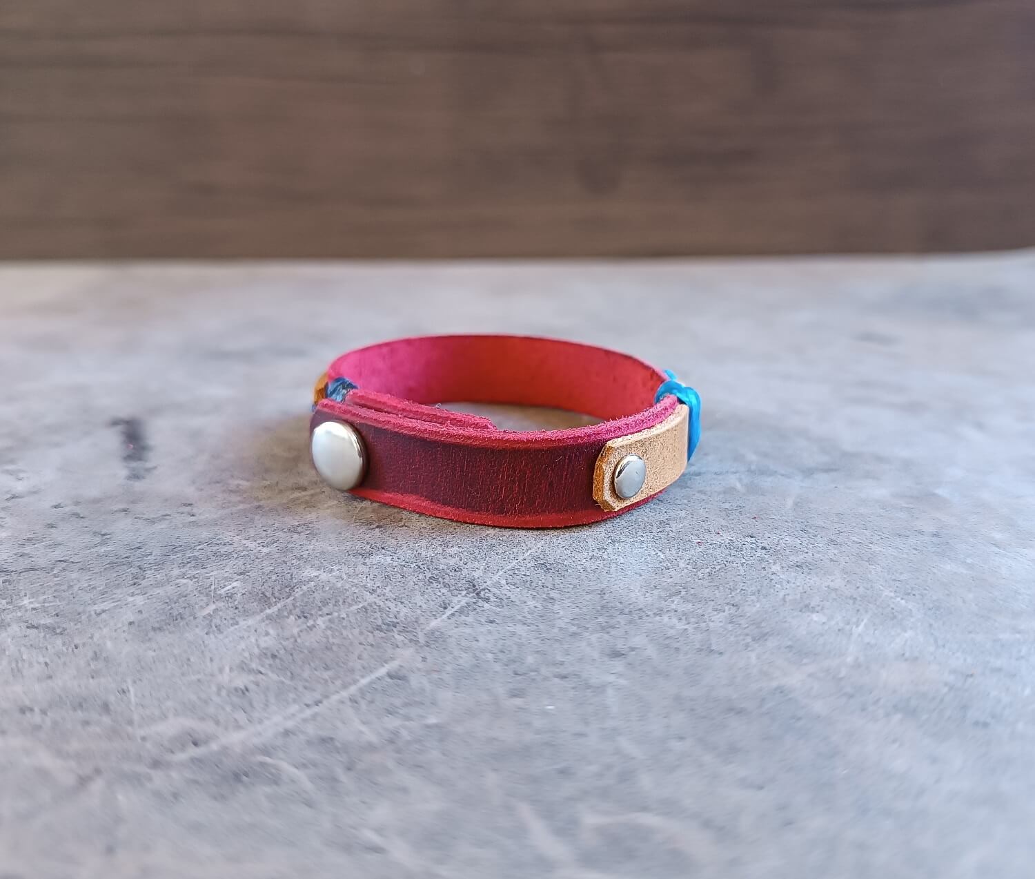 Red leather bracelet with metal clasps on a gray surface