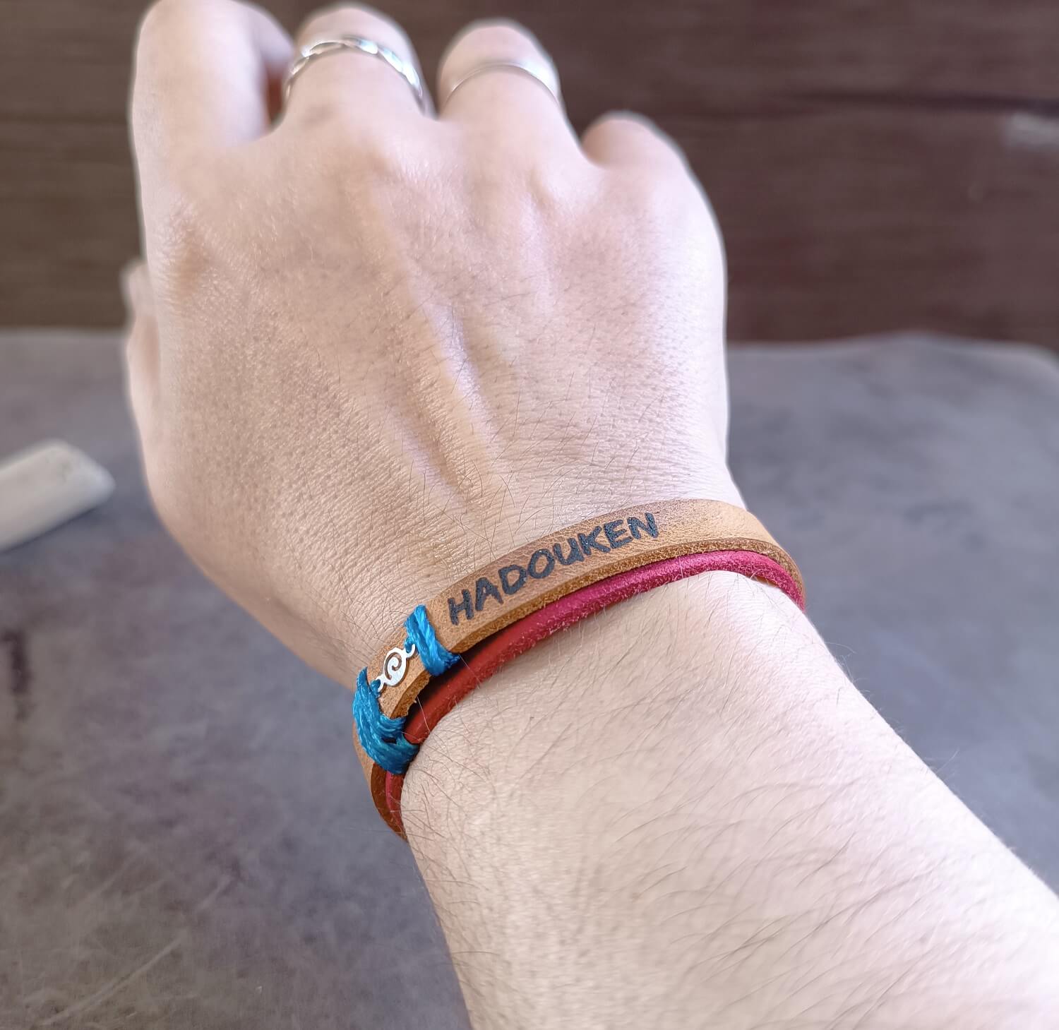 Hand wearing a colorful bracelet with 'HADOUKEN' engraving