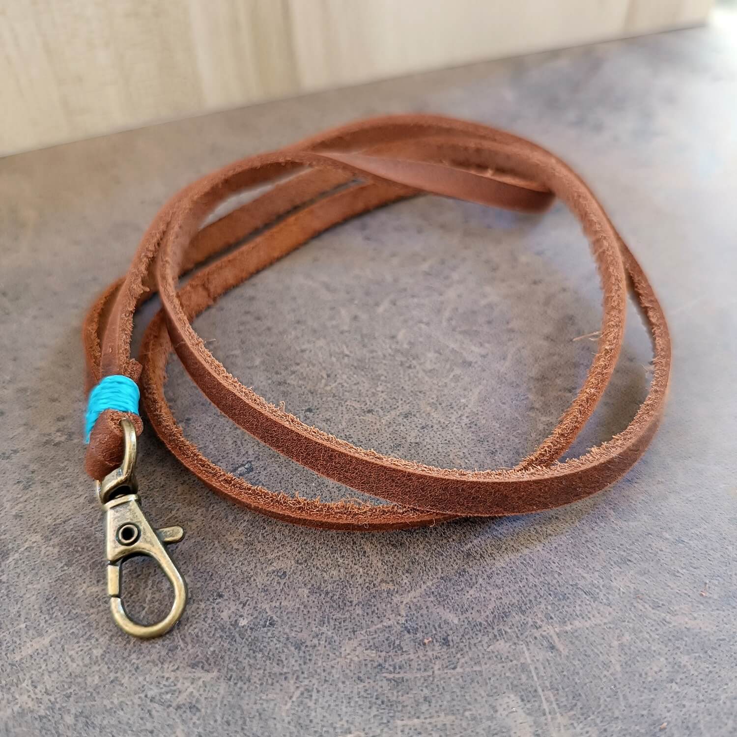 Brown leather lanyard with brass clasp on a gray surface